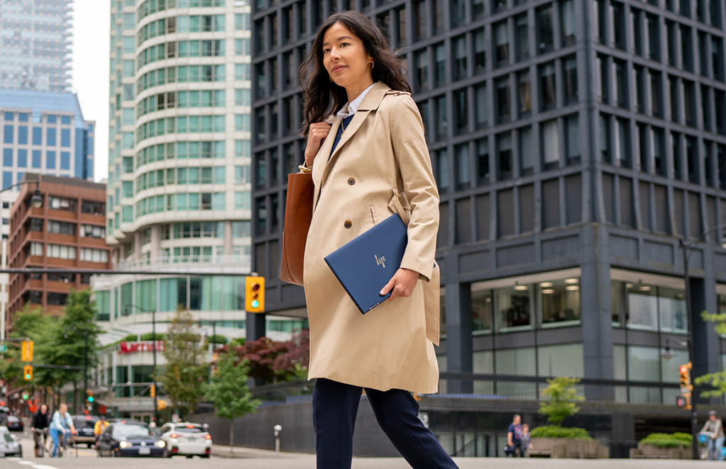 Woman walking down street, holding a Elite laptop