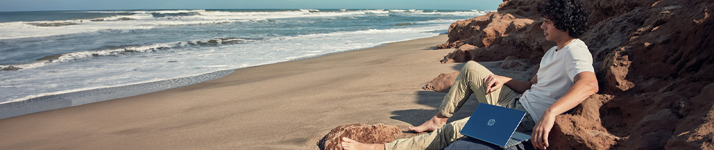 man sitting on a rock by the sea with his HP laptop