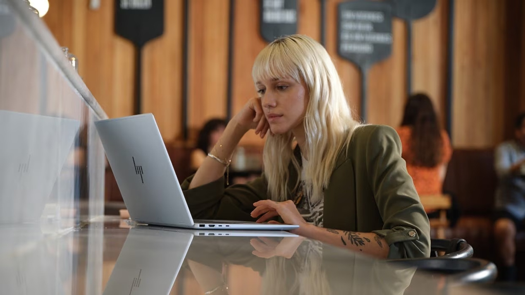 Woman using an HP Envy x360 laptop on a restaurant table.