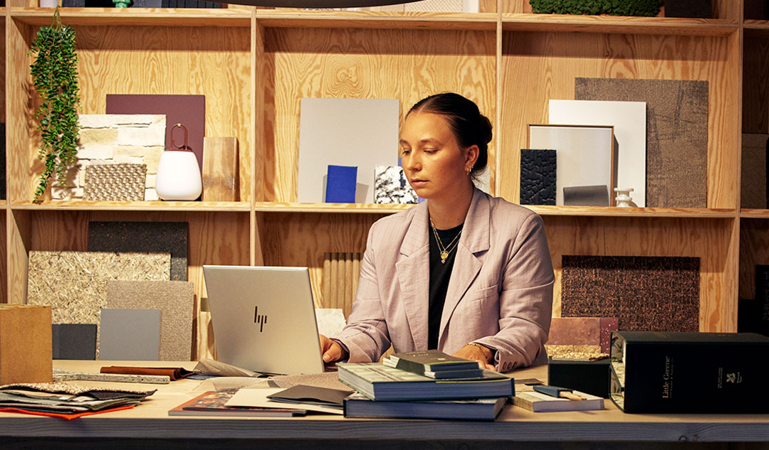 Two coworkers collaborate at a desk, surrounded by plants, a laptop, and a printer in a modern office space.