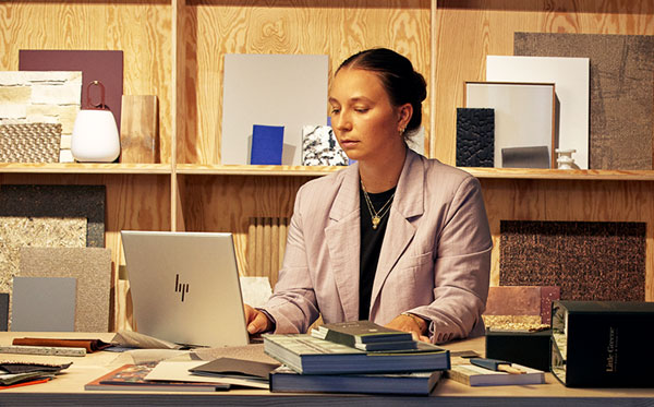 Two coworkers collaborate at a desk, surrounded by plants, a laptop, and a printer in a modern office space